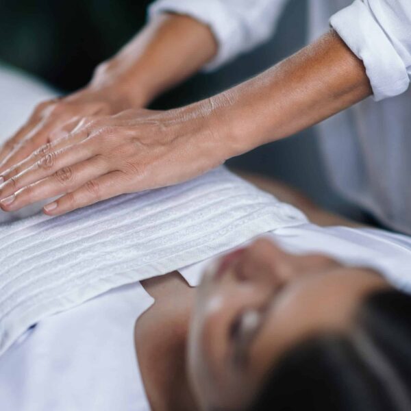 Horizontal image of female Reiki therapist holding hands over patient chest healing heart chakra. Peaceful beautiful teenage girl lying with her eyes closed.